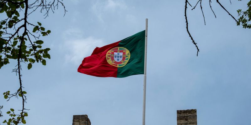 The Portuguese flag on a pole with a serene blue sky background.