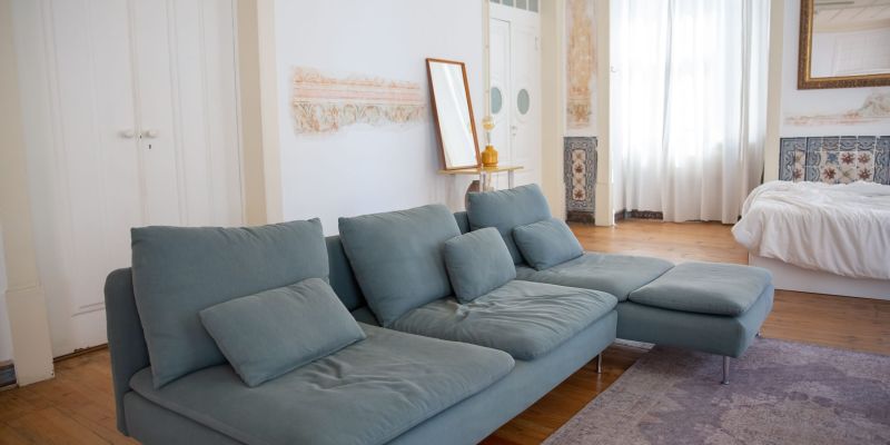 Cozy living room featuring a stylish light blue sofa, wooden floor, and natural light.