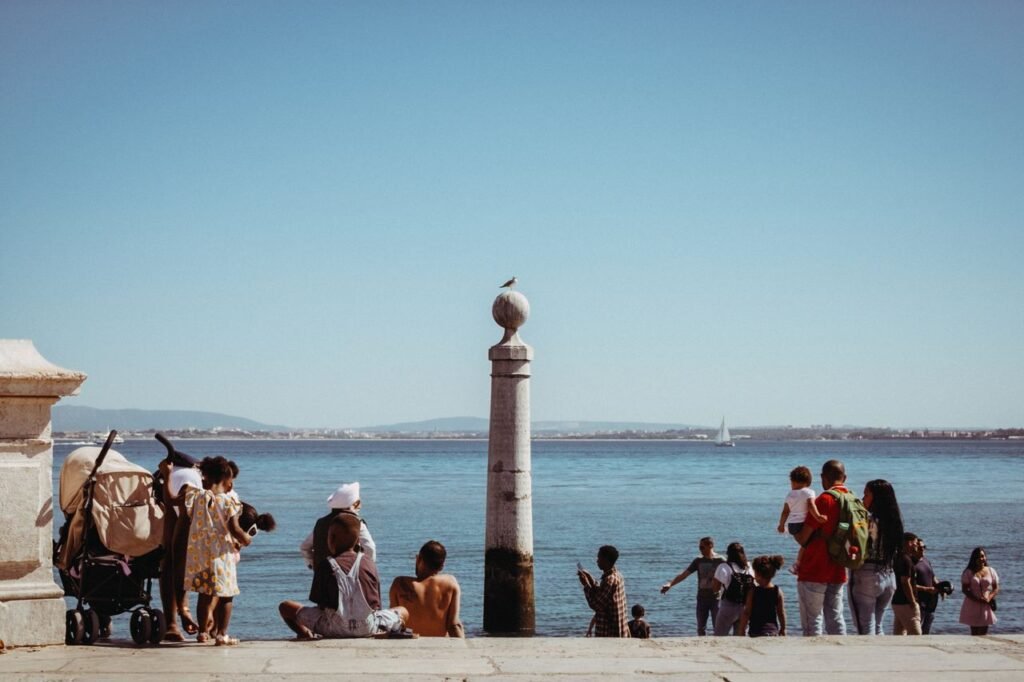 A group of people relaxing by the waterfront in Lisbon, Portugal with a clear sky and sea view.